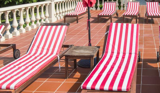 Leere Holzliegestühle mit rot-weiß gestreiften Matratzen stehen in einer Reihe. Luxus im Freien, Sonnenschein. - Foto, Bild