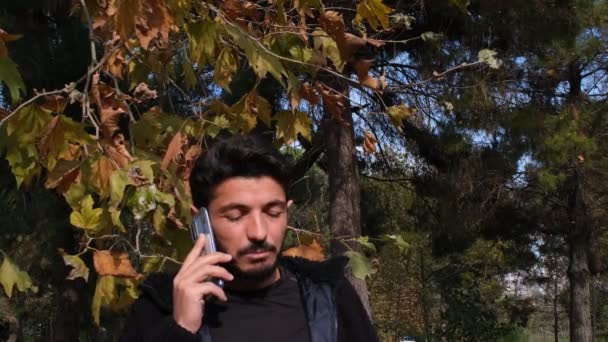 hablando por teléfono, joven hablando por teléfono delante de los árboles, otoño - Metraje, vídeo
