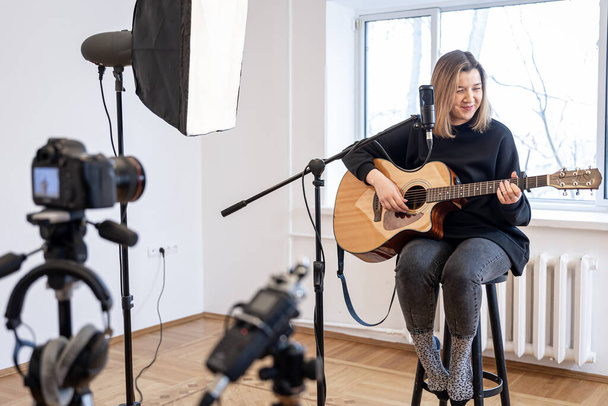 Ένα νεαρό κορίτσι παίζει κιθάρα, ηχογραφώντας βίντεο και ήχο. - Φωτογραφία, εικόνα