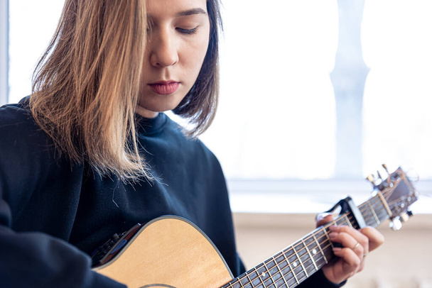 Vakava nuori nainen soittaa akustista kitaraa kotona. - Valokuva, kuva