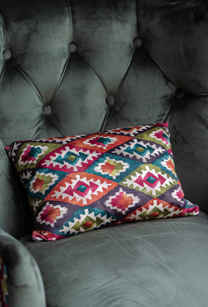 Яркая декоративная подушка с геометрическим дизайном на зеленом кресле. - Фото, изображение