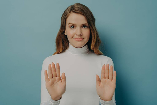 Ελκυστική νεαρή εστιασμένη γυναίκα δείχνει στάση χειρονομία, λέγοντας όχι, απομονωμένη πάνω από το μπλε φόντο στούντιο - Φωτογραφία, εικόνα