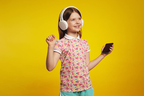 Girl with smartphone and white headphones, listening music and dancing - Фото, изображение