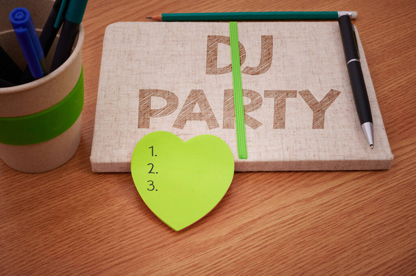 Znak tekstowy pokazujący DJ Party. Koncepcja oznacza osobę, która wprowadza i odtwarza nagraną muzykę popularną w radiu Plain Blank Open Notebooks With Stack Of Pens Container Over Table. - Zdjęcie, obraz