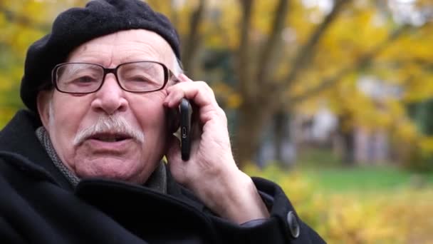 Un abuelo con bigote gris y una boina negra está hablando en un smartphone  - Imágenes, Vídeo
