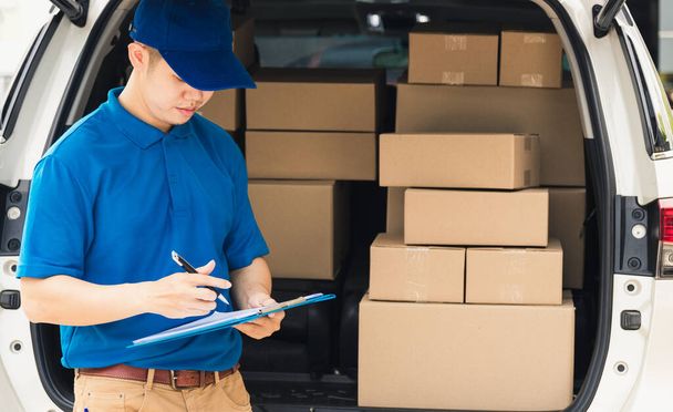 Asian young delivery man courier in uniform hold documents clipboard checking list parcel post boxes near a car for service shipment to customer, Online shopping service concepts - Foto, afbeelding