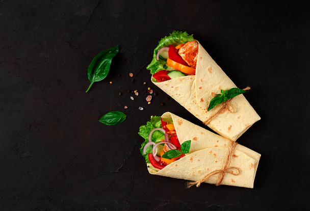 Tortilla wraps, grilled Mexican chicken with vegetables, burritos, on a black table, without people, - 写真・画像