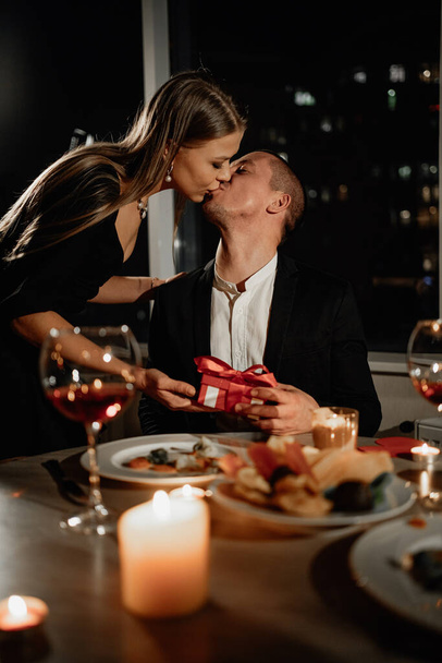 Passionate kiss on a date man and woman, Valentine's Day festive dinner for two, a gift to a loved one, wedding anniversary husband and wife in the evening at home - Photo, Image