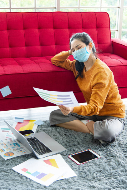 Concept de travail à domicile. Jeune asiatique belle femme en utilisant un ordinateur portable avec gadget tout en étant assis sur un tapis gris à la maison. Femme d'affaires lisant le rapport de vente infographique. - Photo, image