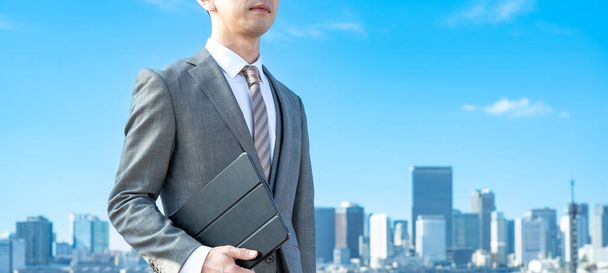 Een zakenman tegen de achtergrond van de blauwe lucht en gebouwen - Foto, afbeelding