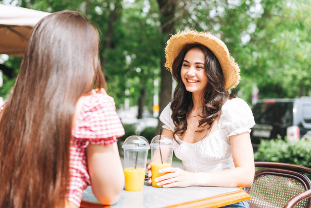 Glücklich lächelnde schöne brünette junge Frauen mit Gesprächen auf der Terrasse des Sommercafés. Unbekümmerte Mädchen in lässiger Kleidung im Urlaub in der Ferienstadt - Foto, Bild