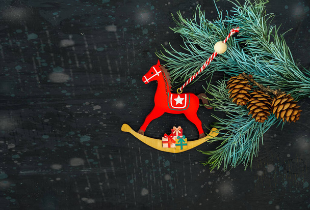 New Year greeting card with a fir branch and a Christmas toy wooden horse on a black background - Photo, Image