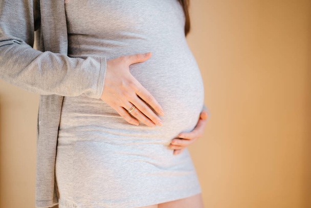 妊娠中の女性はおなかを抱えて壁のそばに立っている。サイドビュー - 写真・画像
