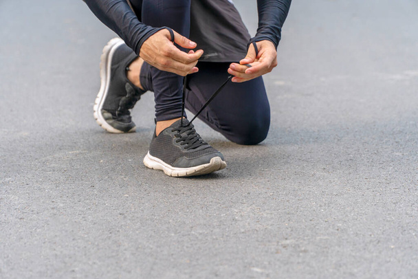 Руки бегуна молодой человек завязывая шнурки на дороге во время тренировки в парке. Здоровые упражнения удобная концепция спортивной обуви. - Фото, изображение