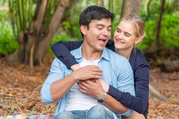 Fröhliche Frau mit blonden Haaren umarmt ihren Freund, während sie im Park sitzt. Romantisches junges Paar, das sich umarmt und lacht, während es sich im Freien anschaut. Valentinstag-Konzept. - Foto, Bild