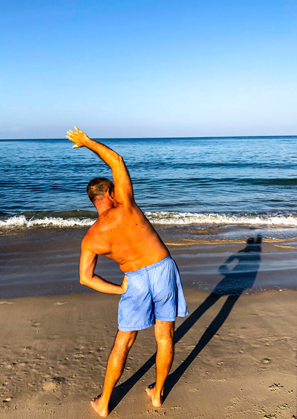 a man goes in for sports, does exercises on the seashore - Фото, изображение