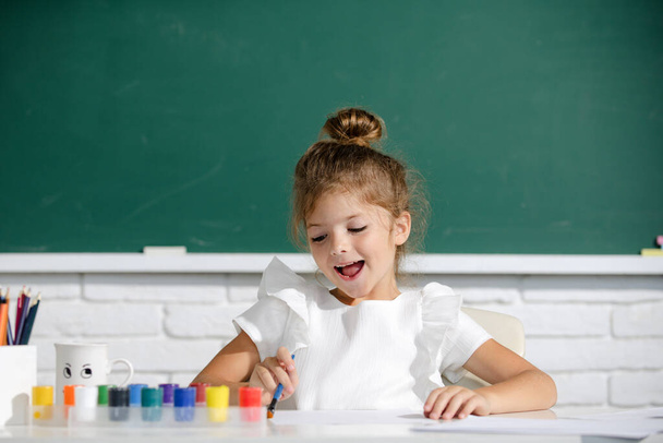 Cute little preschooler child girl drawing at school. Child painting on elementary school. Cute school girl drawing in class at school. - Фото, зображення
