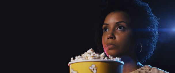 Young woman watching a movie at the cinema and eating popcorn, entertainment concept - 写真・画像