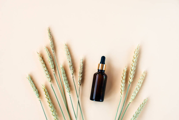 Cosmetic serum in brown glass bottle and spikelets of wheat on a light beige background. Natural cosmetics concept. Top view, flat lay, copy space. - Φωτογραφία, εικόνα
