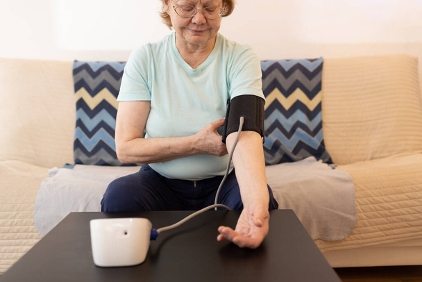Ηλικιωμένη γυναίκα που λαμβάνει μέτρα την αρτηριακή πίεση στο σπίτι. Αυτοφροντίδα της υγείας των ηλικιωμένων - Φωτογραφία, εικόνα