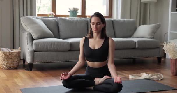 Millennial lady practicing yoga at home meditate in lotus pose - Filmati, video