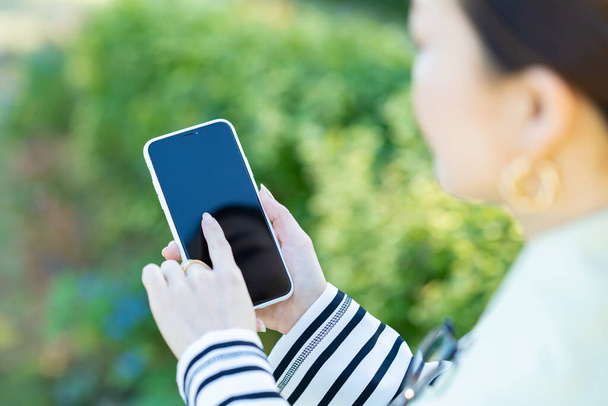 a woman holding a smartphone outdoors - Photo, Image