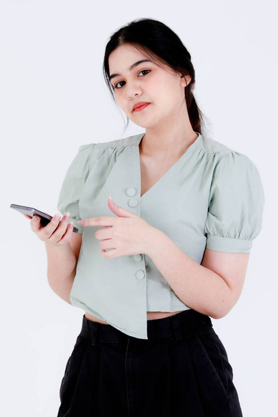 Studio shot of Asian young teen female model with ponytail hair wear dental care teeth braces and crop top outfit standing waving hand greeting say hi on smartphone video call on white background. - Photo, Image
