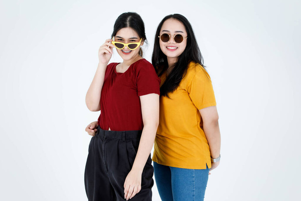 Portret studio shot van twee Aziatische jonge cool modieuze stijlvolle vrouwelijke modellen in casual outfit dragen aanraken mode zonnebril staande taille samen te kijken naar de camera op witte achtergrond. - Foto, afbeelding