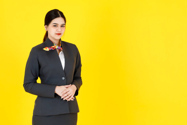ポートレートスタジオショットのアジアのプロ成功したスマート自信のある女性客室乗務員航空ホステスで正式な制服スーツでスカーフ立って笑顔見ますでカメラポーズ黄色の背景. - 写真・画像