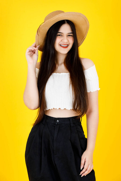 Portrait studio shot of Asian young beautiful sexy long black hair female model wearing crop top outfit dental care braces standing smiling holding hand touching adjusting hat on yellow background. - Fotoğraf, Görsel