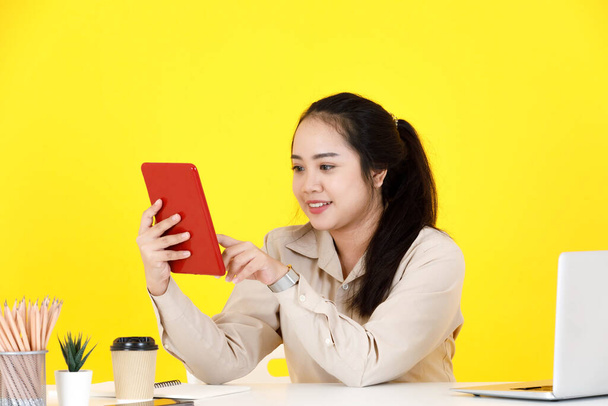 Asyalı tombul kadın sekreter, dokunmatik ekranlı tablet tutarak el sallayarak müşteriyle el sallarken, sarı arka planda video görüşmesinde müşteriyle vedalaşıyor.. - Fotoğraf, Görsel