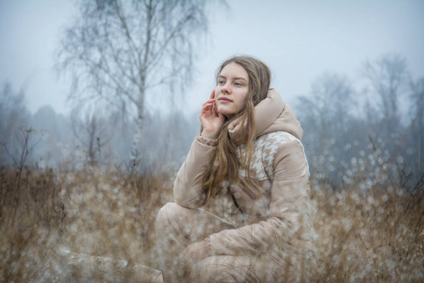 Im Herbst an einem kalten frostigen Morgen auf dem Feld, ein Mädchen mit langen Haaren im Gras mit Tautropfen. - Foto, Bild