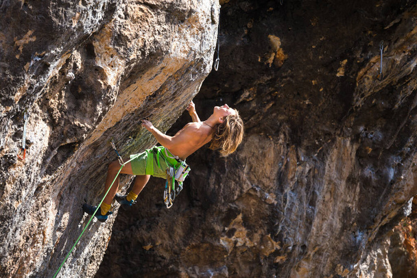 Ein junger Sportler klettert auf einen Felsen, ein Kletterer trainiert im natürlichen Gelände, ein Mann trainiert Kraft und Ausdauer, Klettern für Kinder und Jugendliche. - Foto, Bild