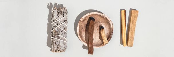 Gegenstände für spirituelle Reinigung - Salbeibündel, Palo Santo Räucherstäbchen und Quarzkristall auf grauem Hintergrund. Ansicht von oben. Banner - Foto, Bild