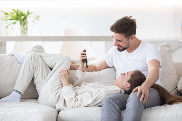 Couple relaxing in living room and smiling looking at smartphone - Foto, Imagen
