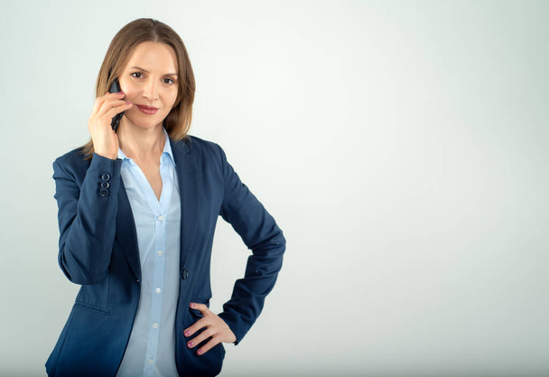 Joven mujer de negocios habla en un teléfono celular aislado sobre fondo gris - Foto, Imagen