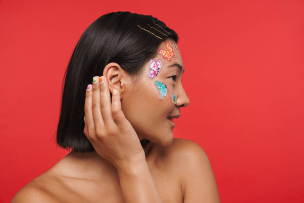 Beauty portrait of a young brunette asian woman with makeup facial decoration over red wall background side view - Φωτογραφία, εικόνα