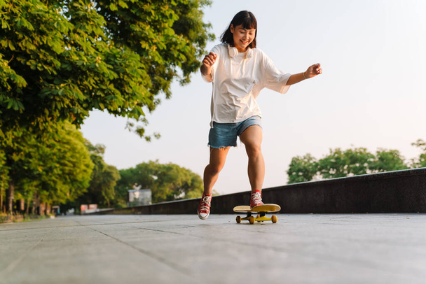 Happy young asian woman riding on a skateboard in the green park - Foto, Imagen
