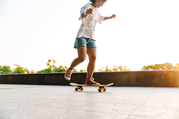 Happy young asian woman riding on a skateboard in the green park cropped - 写真・画像