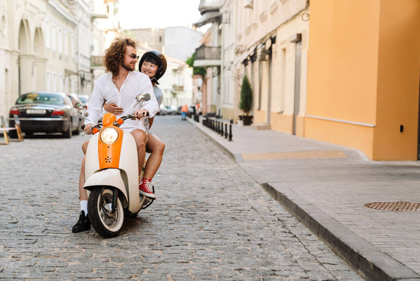 Happy young multiethnic couple on scooter enjoying ride on a street - Foto, immagini