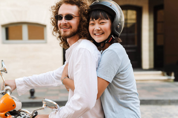 Happy young multiethnic couple on scooter enjoying ride on a street close up - Photo, Image