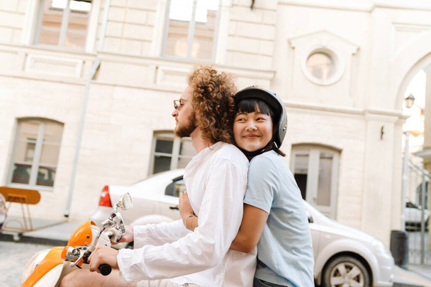 Happy young multiethnic couple on scooter enjoying ride on a street - Photo, Image
