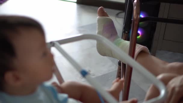 Foco seletivo da perna quebrada com bandagem de gesso cuidar da criança na cadeira do bebê - Filmagem, Vídeo