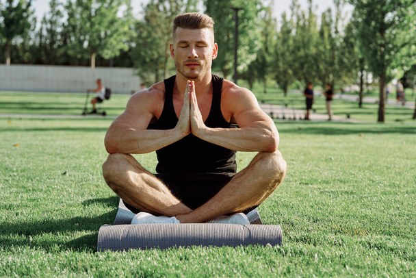 sporty man sitting on the lawn in the park training - Foto, Imagem