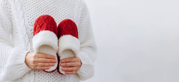 Femme en pull blanc tient chaud chaussons rouges tricotés. Concept de maison famille vacances douillettes Noël Nouvel An. - Photo, image