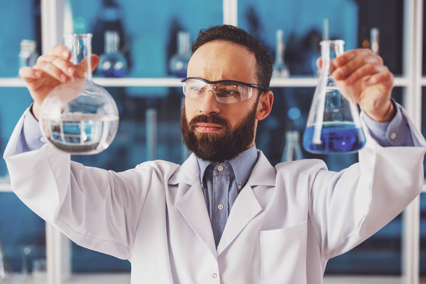 Komea miespuolinen tutkija turvalaseissa havaitsemassa nestettä pulloissa laboratoriossa
. - Valokuva, kuva