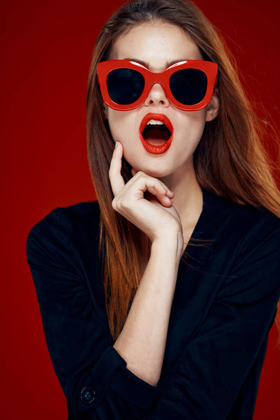 bella donna indossare occhiali da sole moda posa acconciatura sfondo rosso - Foto, immagini