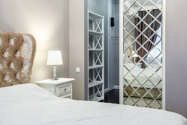 豪華なアパートで現代的なベッドルームのデザイン。冷たいトーン、塗装グレーの壁、ミラーとドアのワードローブ. - 写真・画像