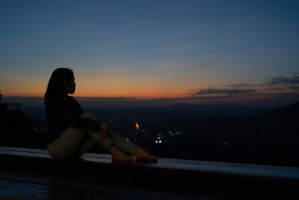 Silhouette einer Frau, die auf der Terrasse sitzt und den Sonnenuntergang über dem Berg betrachtet - Foto, Bild