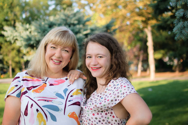 Female portrait of a beautiful plus size blond, blue-eyed mother and daughter in the park during summer. Family day, happy people concept - Photo, Image
